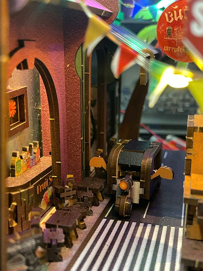 A miniature diorama model of a street scene with a small motorcycle, tiny figures, a bar with bottles, and colorful hanging flags in the foreground.
